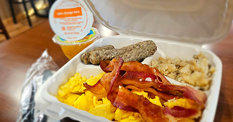 Bacon and eggs in a to go container with orange juice